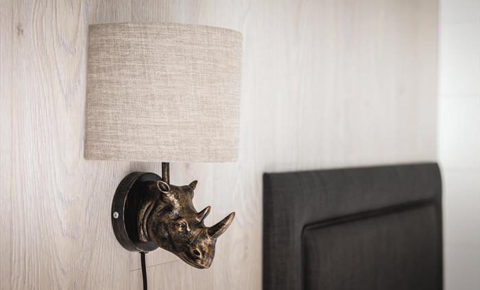 Wall-mounted bedside lamp with a bronze rhino head and grey lampshade.